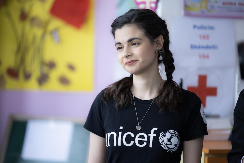 Wearing a UNICEF logo T shirt, Aria Mia Loberti smiles while listening to UNICEF staff and partners introduce children’s educational programming in Kosovo. 